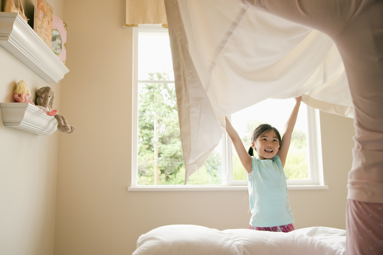 little girl helping put sheets on bed