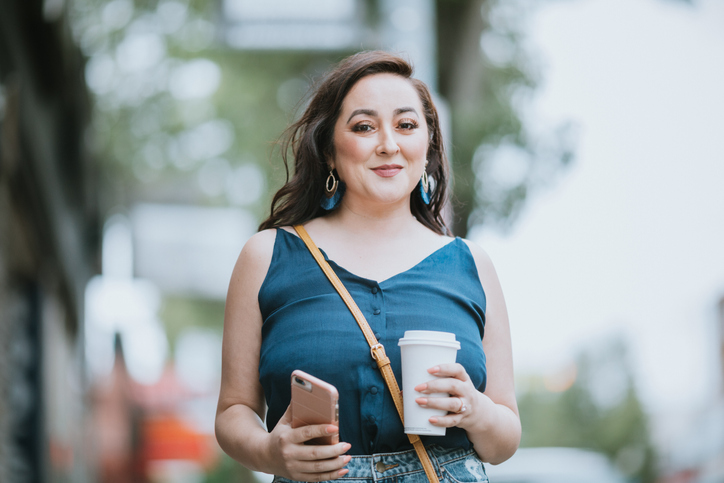 A fashionable young woman strolls the Seattle sidewalks and holds a paper coffee cup.