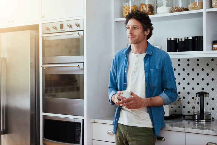 A man clutches a cup of coffee near his refrigerator
