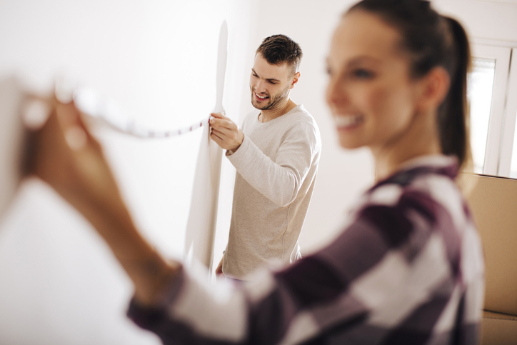 young couple use measuring tape to measure wall space in new home