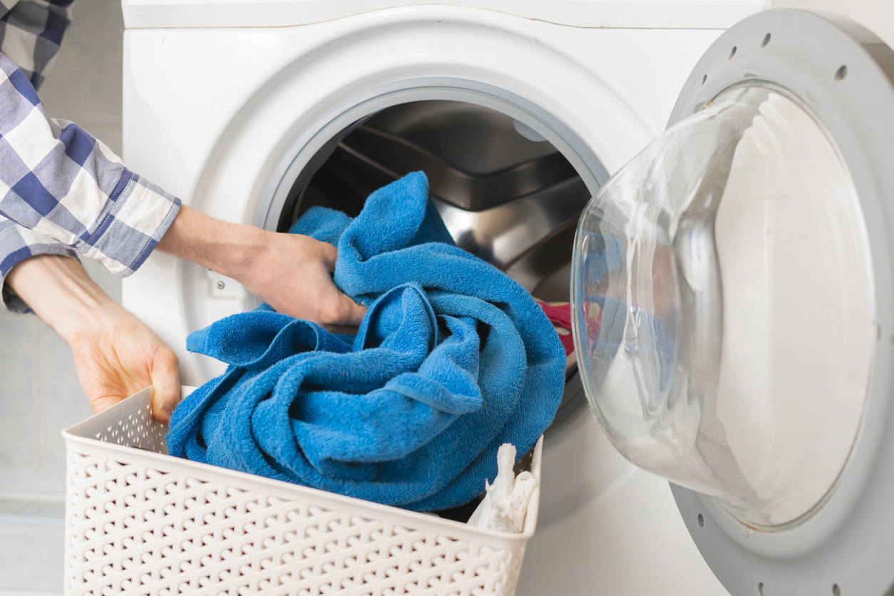 a person’s hand puts dirty clothes in a front-loading washer