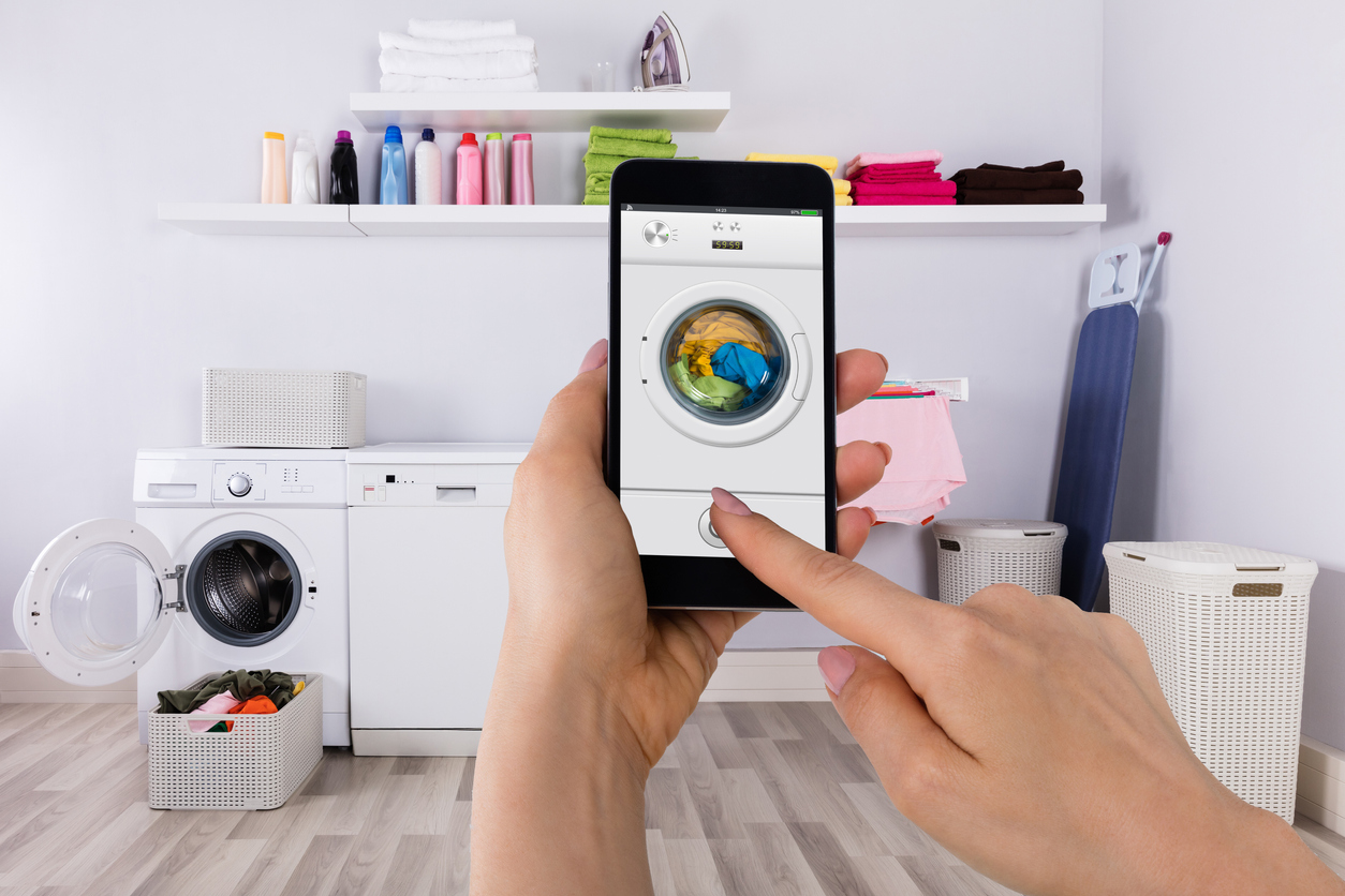 a person’s hand manages the laundry with a smartphone