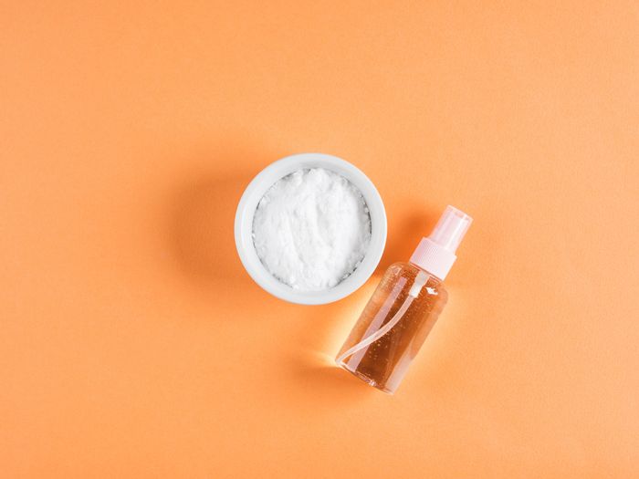A bowl of baking soda and a spray bottle of essential oil on an orange background