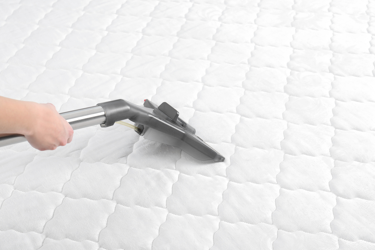 a hand holding a vacuum cleaner on a matress