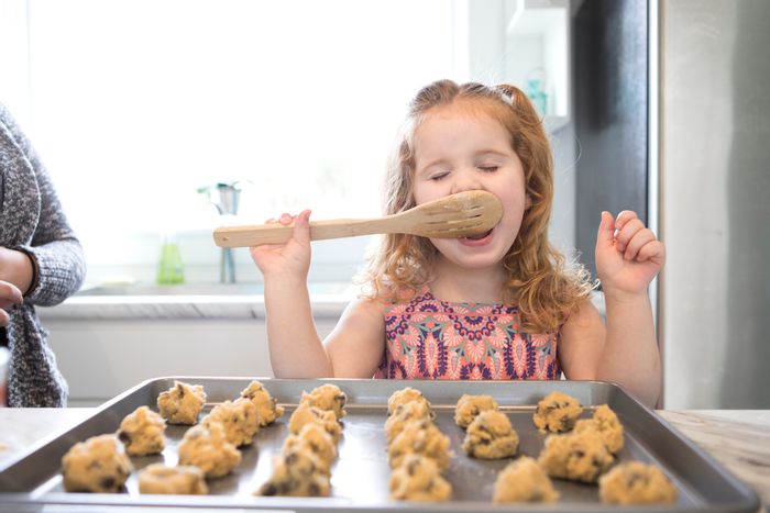 little girl licks spoon while making cookies