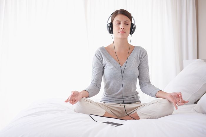 a woman sits cross-legged on her bed as she listens to a yoga podcast