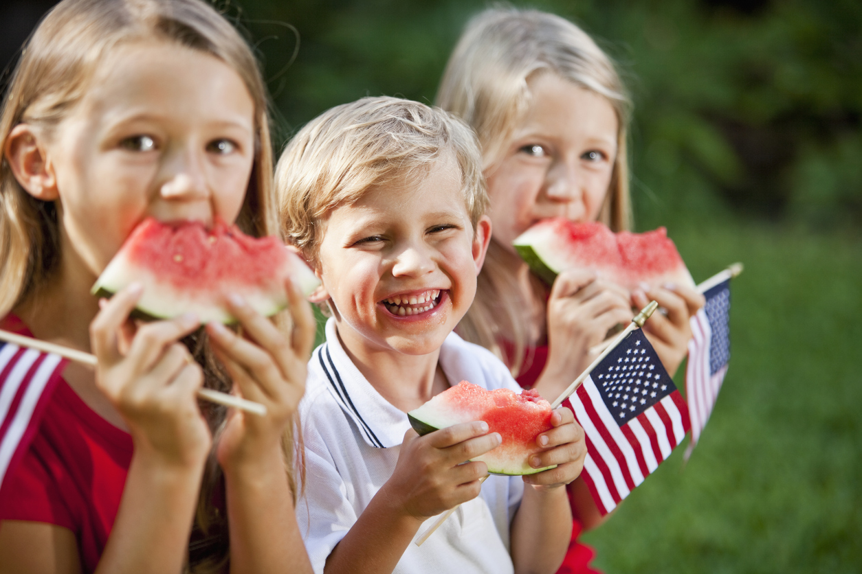 three kids holding small American flags and eating watermelon slices