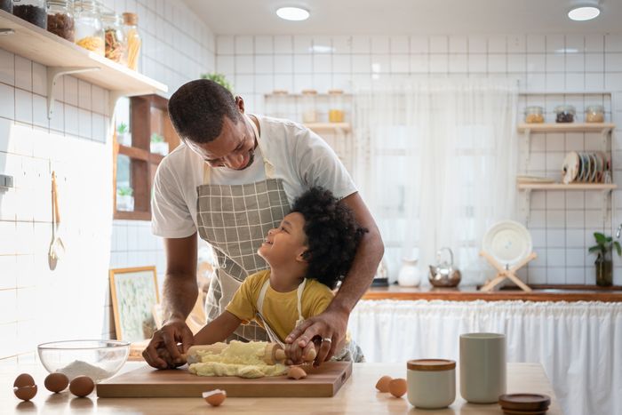 Dad and kid use rolling pin on cookie dough in bright kitchen