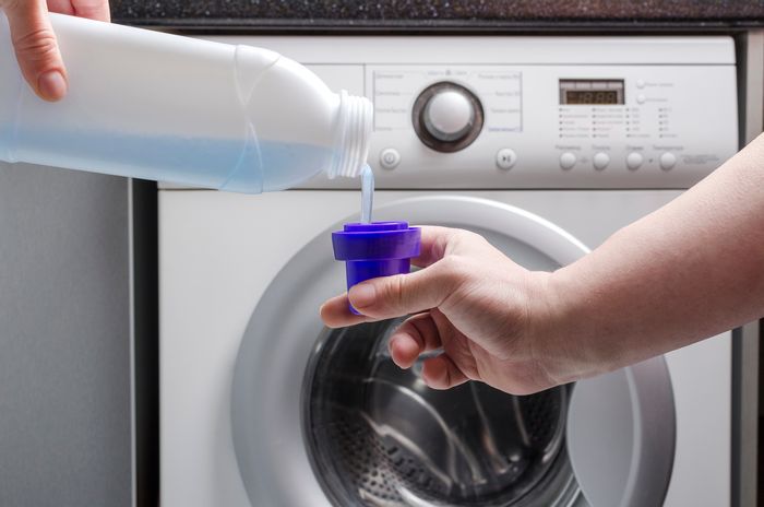 a pair of hands pours liquid detergent in cap in front of washer