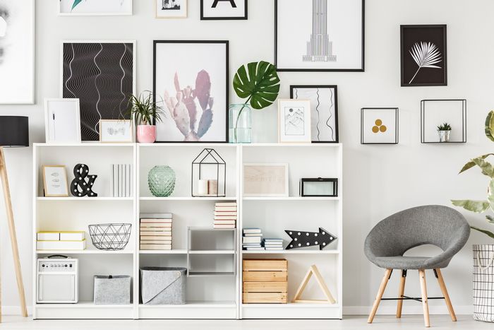 White living room with grey chair, wall art, bookshelf, and stylish storage 