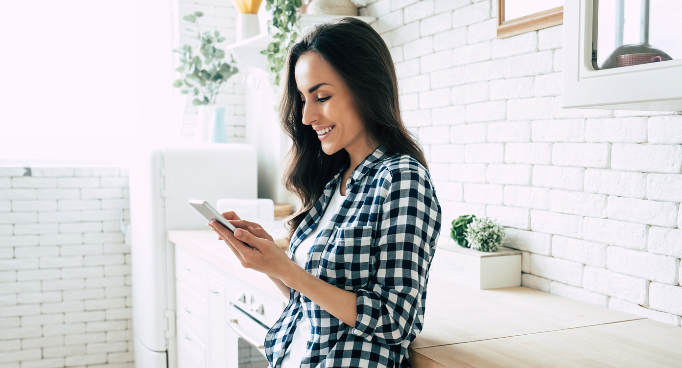 woman smiling and looking at her phone in a white kitchen 