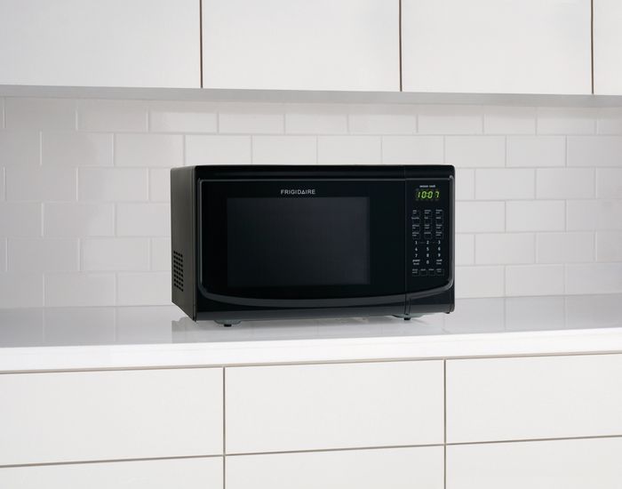 Black Frigidaire microwave sitting on a white countertop in a white kitchen.