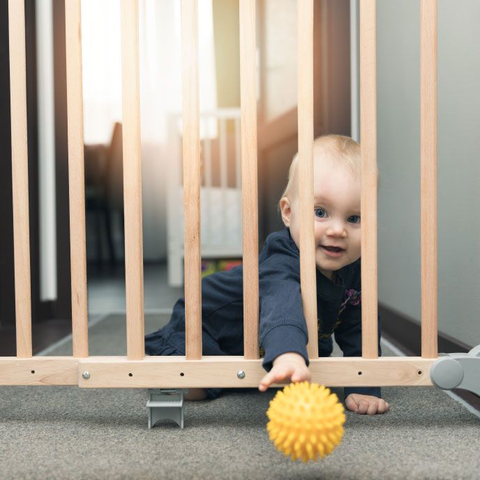 Baby playing with a ball on the opposite side of a baby gate.