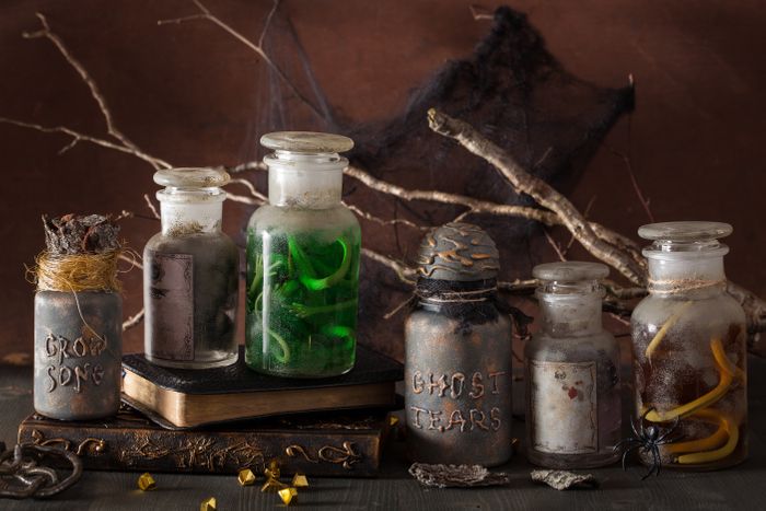Dusty potion bottles with spell books, branches, and cobwebs on a table.