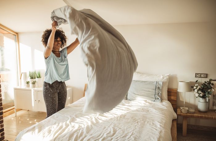 Woman shakes out her comforter as she makes her bed 