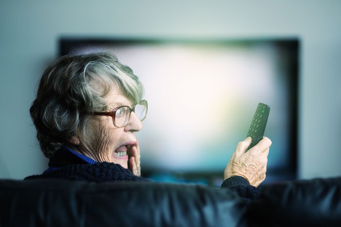 An older woman looks surprised at a television remote.