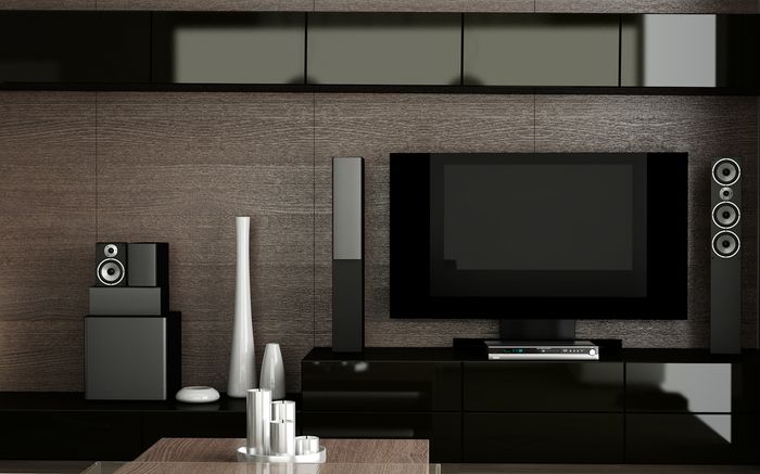 A modern-styled living room with dark wood and high-tech television screen and speakers.
