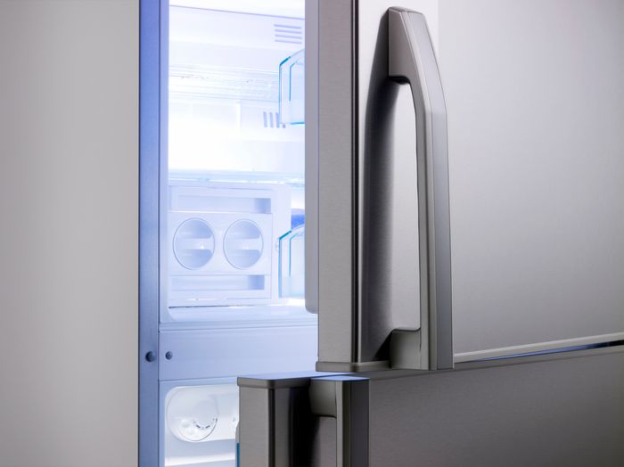 A closeup of a stainless steel refrigerator, open just a crack and completely empty and clean inside.