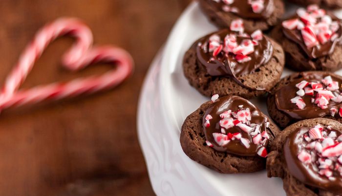 Chocolate cookies with crumbled candy canes on top sit in a neat stack on a plate.