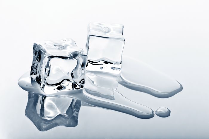 Two ice cubes melting on a reflective silver surface.