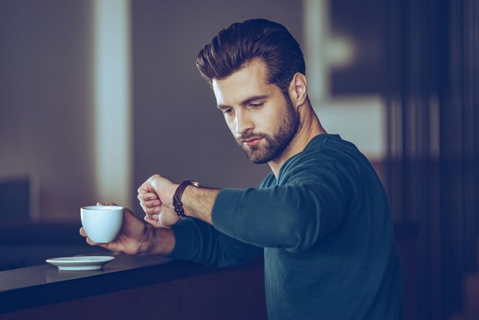 A man checking his watch in a coffee shop, with a cup of coffee in hand.