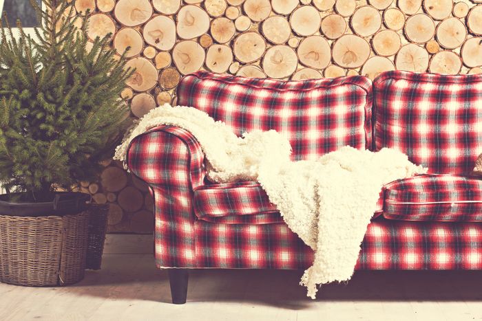 A red tartan couch in front of a wall made of wooden log cross-sections.