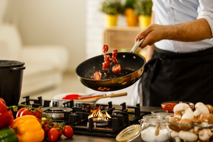 A chef tosses vegetables on a skillet over a cooktop.