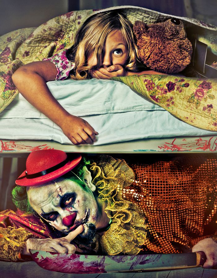 Young girl hiding in bed with a teddy bear. A creepy clown with a bloody knife peeks out from underneath her bed, holding up his finger in a "shh" motion.