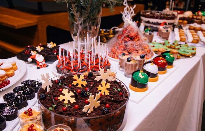 A long, white tableclothed buffet of holiday-themed desserts.