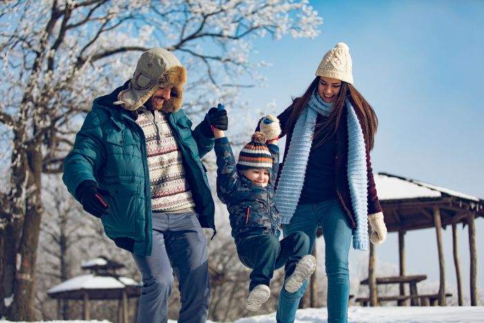 A young couple bundled up in winter clothes hold hands with their similarly dressed child.
