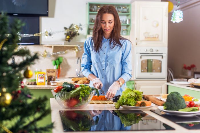 A woman chops carrots, surrounded by plates full of vegetables on her countertop. An induction cooktop is on the counter nearby her.
