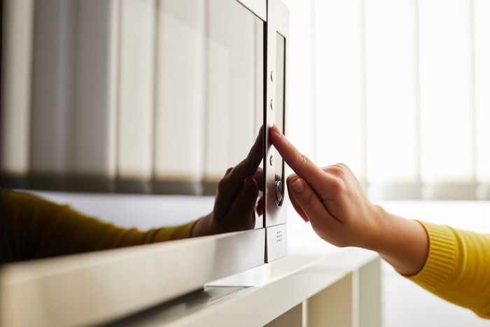 A woman's hand reaches out to touch a button on a stainless steel microwave.