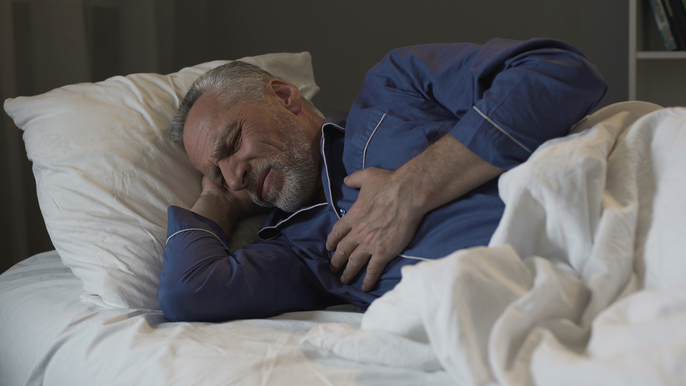 man sleeping on side has hand on chest and looks uncomfortable