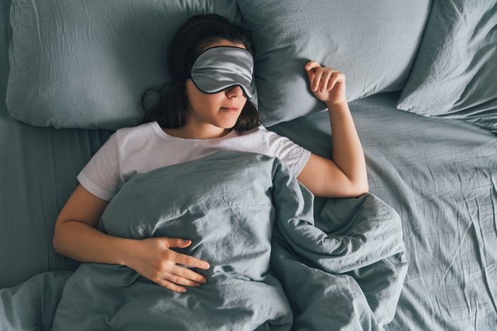 A woman lies in bed with a silk mask covering her eyes.