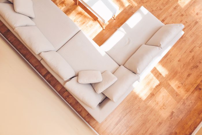 An overhead shot of a beige sectional with a wood floor underneath in a sunlit living room.