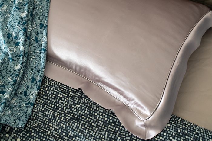A pink silk pillow on a bed with brown sheets and a polka dot bedspread.