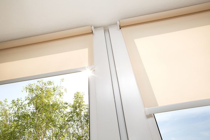Low angle shot of two half-open window shades, with bright sun streaming in through them.