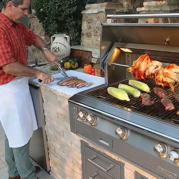 View of a man cooking on an Alfresco grill in a modern backyard kitchen