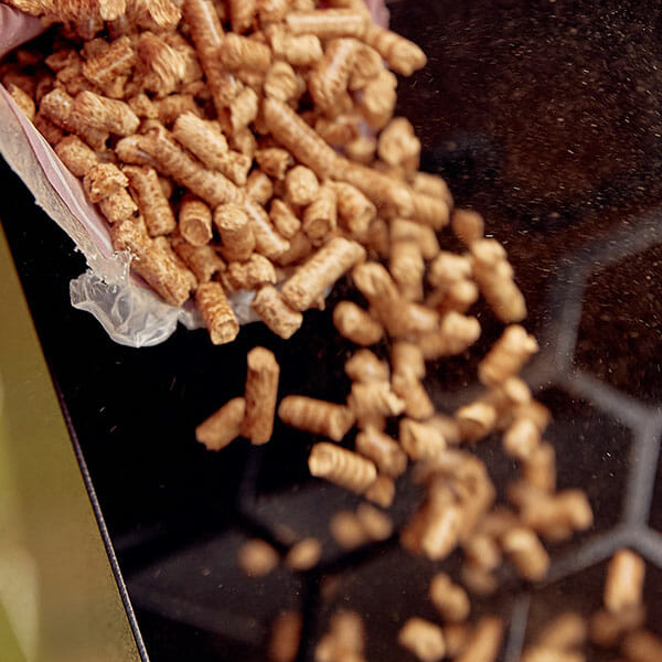 Close view of a scoop of wood pellets being pored into a grill