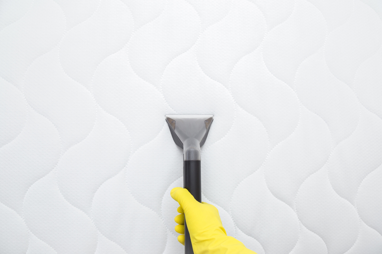 Close-up of a gloved hand vacuuming a mattress