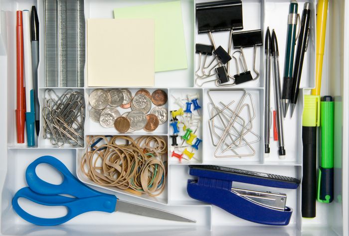 An overhead shot of a white drawer divider, full of office supplies organized into separate sections.