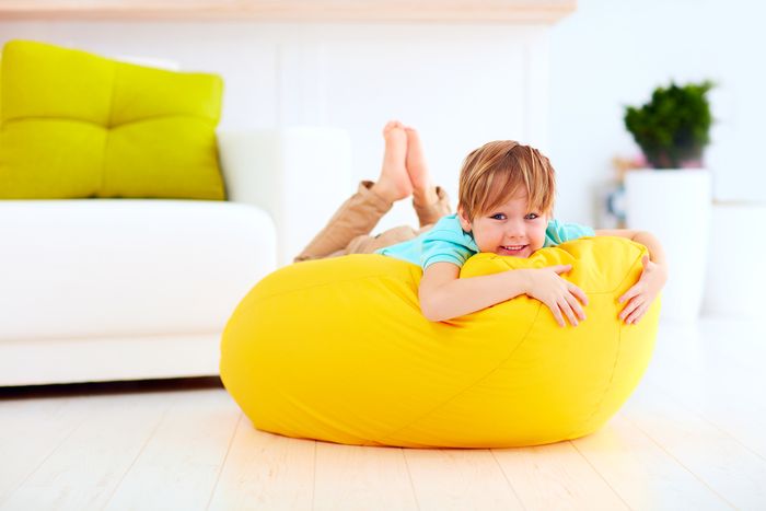 A young boy lays on a bright yellow pouf-style ottoman in a white room.