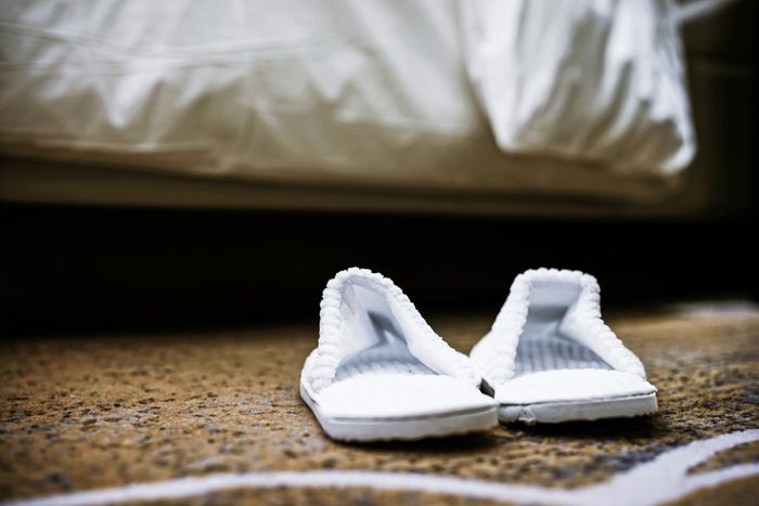 Two white spa slippers wait at the foot of a bed.