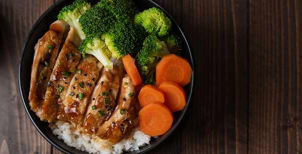 Top view of Homemade Chicken Teriyaki grilled with rice, carrot, and broccoli in a black bowl
