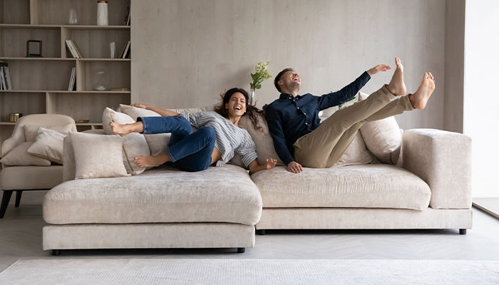 Young man and woman jumping onto a sectional sofa living room