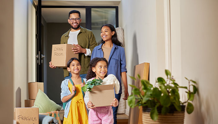 Family carrying moving boxes labeled living room into their new home