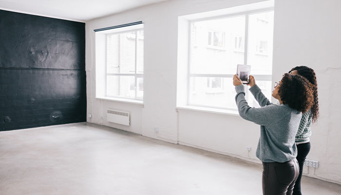 Two women photographing an empty room with a tablet to plan the furniture layout