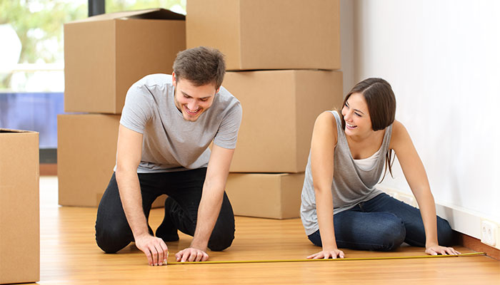 Couple measuring the floor with a tape measure among moving boxes in a new home