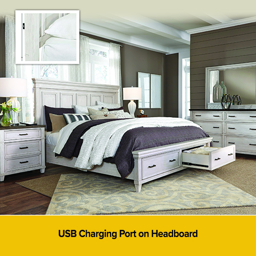 Contemporary bedroom showroom featuring a wood platform bed with a tall wood headboard, white bedding, and layered accent pillows, with a rust-colored throw draped across the foot. Soft under-bed lighting glows along the base, and a matching nightstand and dresser with a mirror and decorative vase sit against dark walls. “Price Plunge” and “While Quantities Last” promotional text appears along the bottom.