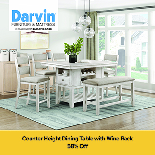 An advertisement for Darvin Furniture & Mattress featuring a white, rustic-style counter height dining set. The set includes a square table with a built-in wine rack and storage drawer, four matching chairs with gray upholstered seats, and a coordinating bench. The furniture sits on a light teal rug in a bright room with large windows. A yellow banner at the bottom states: Counter Height Dining Table with Wine Rack, 58% Off.